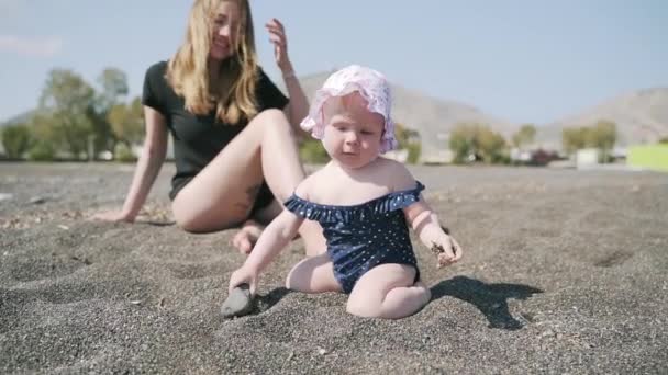 Un disparo alrededor de una madre y una hija pequeña en la playa de arena volcánica — Vídeo de stock