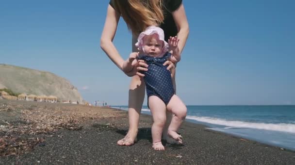 En liten flicka försöker göra sina första steg längs havet kusten på Santorini — Stockvideo