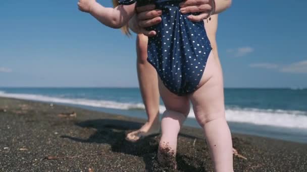 Een vrouw neemt de handen haar kleine dochter aan de zee kust — Stockvideo