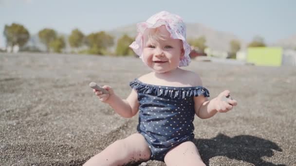 Nahaufnahme eines einjährigen Mädchens, das am Strand mit Steinen spielt — Stockvideo