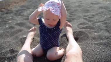 Bir yıllık kız sahilde beyaz şapka çıkarmak için çalışır