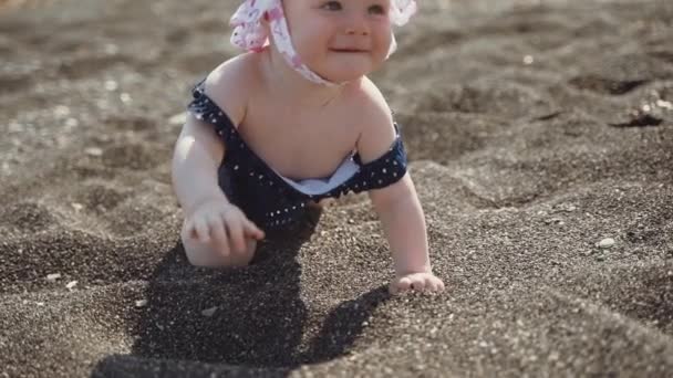 Un plan de cerca de una niña de un año arrastrándose en la playa de arena volcánica negra en la isla de Santorini — Vídeo de stock