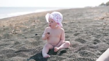 Bir yıllık çıplak kız deniz plajında taşlarla oynar