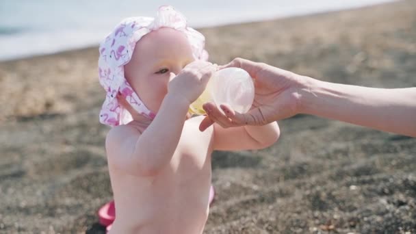 Una niña desnuda bebe de la botella en la playa del mar — Vídeo de stock