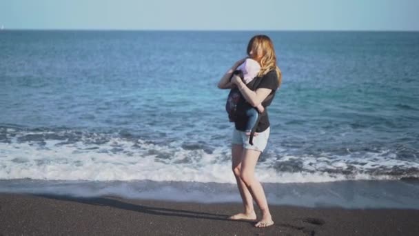 Una madre cerca di mettere il suo bambino in una fionda per dormire vicino al mare — Video Stock