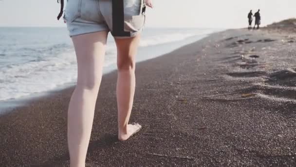 Uma jovem mulher segura seu bebê em uma funda e caminha ao longo da costa do mar — Vídeo de Stock