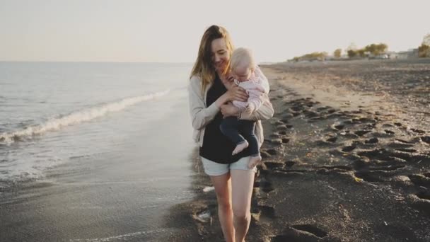 A young woman holds her baby and walks along the sea coast — Stock Video