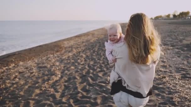 A woman holds her baby and runs along the sea coast — Stock Video