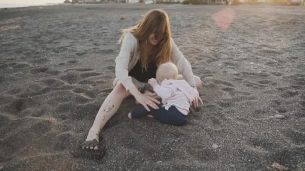 Uma filha de um ano abraça com sua mãe na praia — Vídeo de Stock