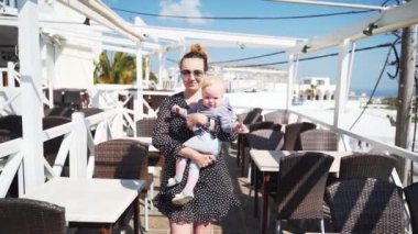 Kucağında çocuklu genç anne, Yunanistan'ın Santorini kentinde denize bakan bir restoranda terasa çıkıyor. Bebekle yürüyüş. Yavaş çekim