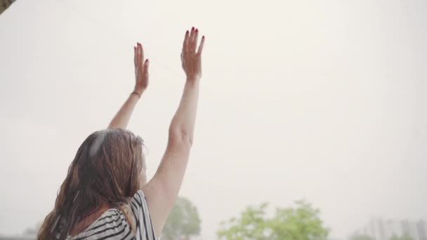 Дівчина з довгим темним волоссям піднімає руки під час лиття дощу, КОЛОШІВ — стокове відео