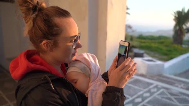 Gün batımında kollarında uyuyan bir bebek ile bir fotoğraf yapar — Stok video