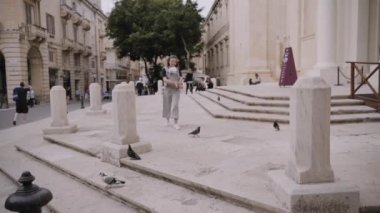 Bebek sapanı olan bir anne, eski şehir Valetta'da güvercinleri yavaş çekimde besliyor.