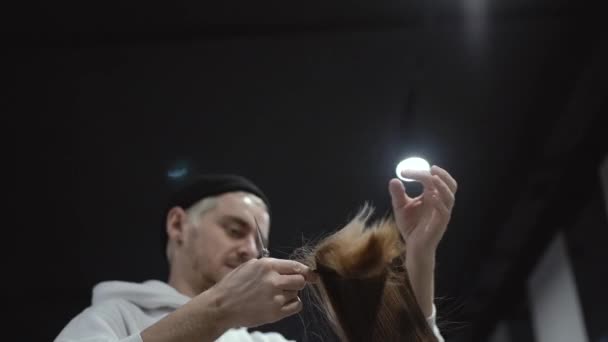 Um cabeleireiro masculino penteia uma fechadura de cabelo loiro — Vídeo de Stock