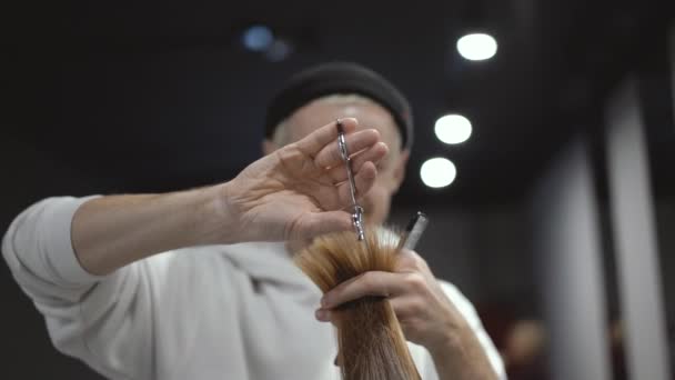 Un plan intermedio de un peluquero macho moliendo un mechón de pelo castaño claro — Vídeo de stock