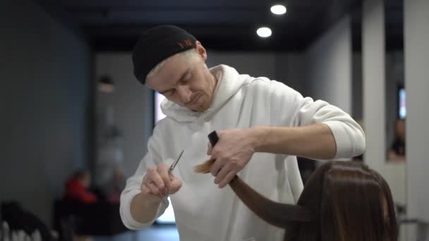Мужчина стрижет, расчесывает и делит переливающиеся каштановые волосы — стоковое видео