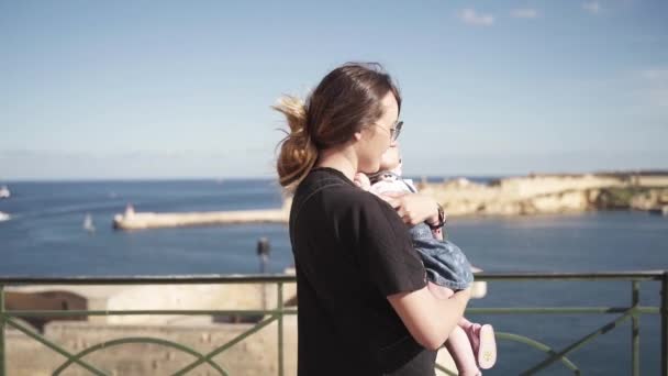 Een middelste plan van een vrouw met haar pasgeboren baby in de buurt van de kust van de zee in een oude stad Valetta wervelende — Stockvideo