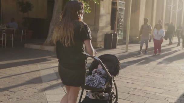 在阳光明媚的日子里，一位母亲带着黑色婴儿车穿过老城区瓦莱塔 — 图库视频影像