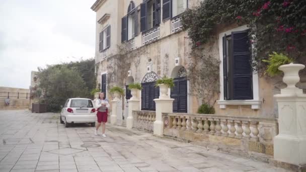 Een moeder loopt met een baby in een slinger door de oude stad Valetta in een warme zomerdag in slow motion — Stockvideo