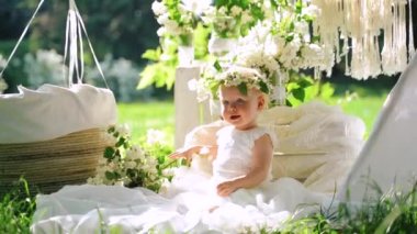 İlk doğum günü. Sevimli bir bebek kız parkta beyaz çiçekler oturur. Yavaş çekim