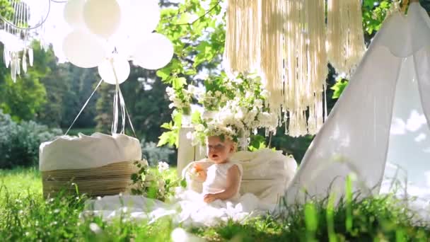 Een foto sessie van een baby in de decoratie met witte bloemen, Wigwam en vliegende ballonnen. Slow Motion. — Stockvideo