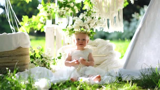 Una niña pequeña se sienta en flores y mordisquea cuentas blancas, 4k — Vídeo de stock
