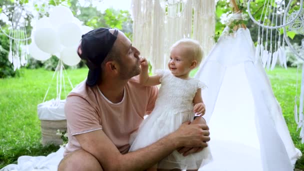 4K Un hombre joven juguetes con una niña de un año en la decoración de flores blancas — Vídeos de Stock