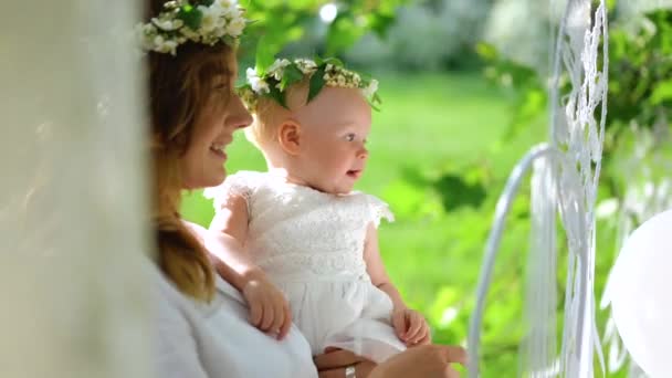 Una joven madre en la corona tiene en las manos a su niña de un año en un vestido blanco. Moción lenta — Vídeos de Stock