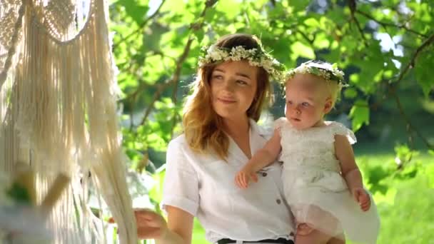 Een jonge moeder en haar dochter in wreathes brengen tijd door in het groene zomerpark in de buurt van Dream Catcher. Gelukkige familie vakantie. Liefde en geluk — Stockvideo