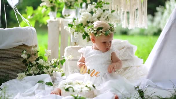 Glückliches Baby in der weißen Geburtstagsblütendekoration im Sommer. Zeitlupe — Stockvideo