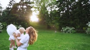 Genç anne ve bebeği yaz gününde doğada gün batımının tadını çıkarıyorlar. mutlu aile açık havada yürüyüş. Anne bebeği havaya savuruyor. Yavaş Çekim 120 fps,