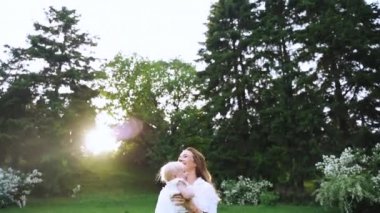 Yeşil parkta annelerin elinden bir bebek atlıyor. Mutlu bir aile tatili. Panoramik Kamera Çekimi.