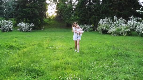 Een jonge moeder loopt met de baby in de zomer groen park in slow motion — Stockvideo