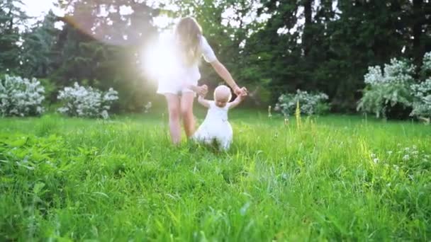 Genç bir anne yavaş çekimde yeşil çimenler üzerinde yürümek için bebek öğrenir. — Stok video