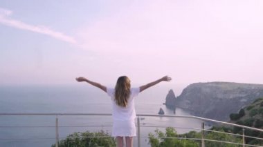 Genç yetişkin kadın, denize bakarak ellerini kaldırdı