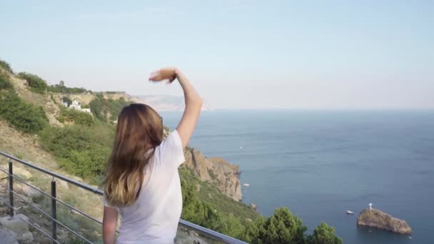 Mujer joven adulta mirando al mar, saludando con la mano — Vídeo de stock