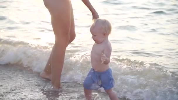 Jovem mãe adulta e seu bebê em pé na água na praia — Vídeo de Stock