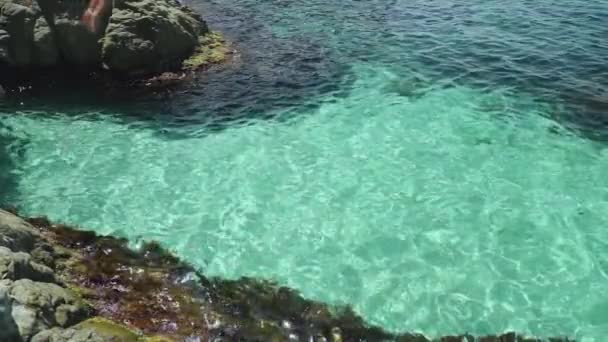 Młody dorosły człowiek skacze w wodzie morskiej ze skały — Wideo stockowe
