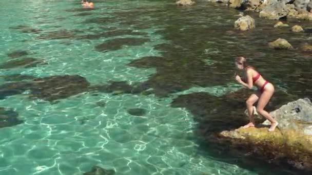 Молода доросла жінка в купальнику стоїть на скелі біля моря — стокове відео