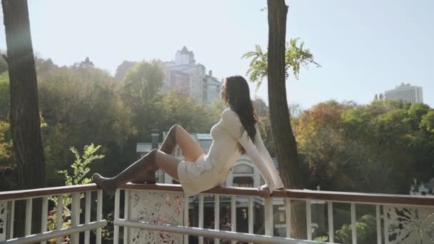 Fiatal felnőtt lány élvezi a városi kilátást, ül a parkban — Stock videók