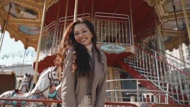 Young adult girl standing near carousel and smiling wide — Stock Video