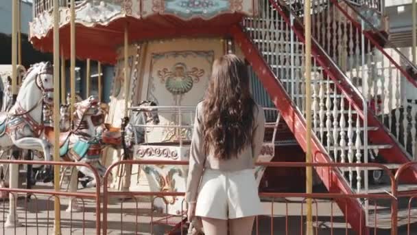 Jong volwassen vrouw staan in de buurt carrousel en glimlachen mooi — Stockvideo