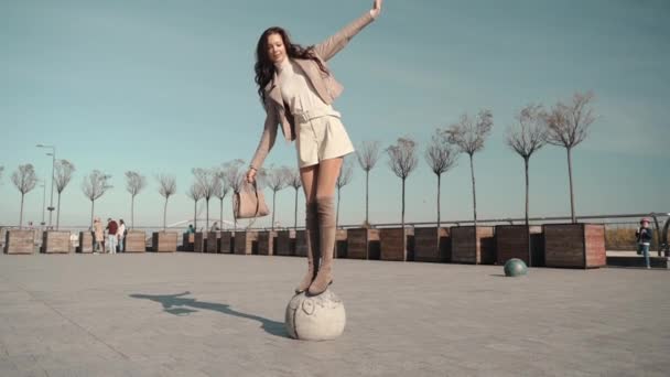 Chica adulta joven sosteniendo el equilibrio y de pie en la plaza de la ciudad — Vídeos de Stock