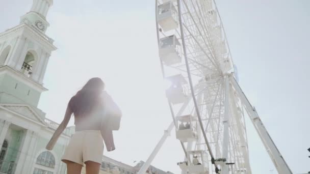 Young adult female standing on city square near ferris wheel — Stock Video