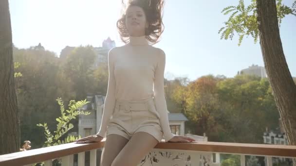 Young adult woman sitting on fence against city on background — Stock Video