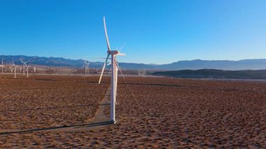 Palm Springs, California yakınlarındaki bir çöl rüzgâr çiftliğinin üzerinden geçen hava görüntüleri, dağlara doğru uzanan uzun bir sıra rüzgar türbini gösteriyor. Kamera yol boyunca uçuyor, bir tanesiyle.