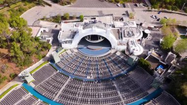 Los Angeles 'taki büyük bir açık hava amfi tiyatrosunun dinamik hava manzarası, simetrik katmanlı koltuklar, süpürücü mimari eğriler ve manzaralı bir tepe arkaplanı. 20 Mart 2025 'te yakalandı.