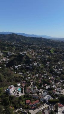 Los Angeles, Kaliforniya 'daki Hollywood Hills' in yemyeşil yerleşim alanının üzerinde uçan dikey bir hava aracı görüntüsü. Zarif villalar ve dolambaçlı sokaklar tepe boyunca yayıldı.