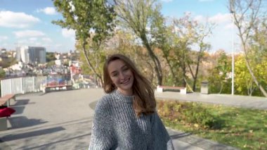 Genç bir kadın, arkasında canlı ve hareketli bir şehir siluetini neşeyle sergileyerek yemyeşil bir parkta yürüyor. Ağır çekim. Kyiv, Ukrayna. Yüksek kaliteli HD görüntüler