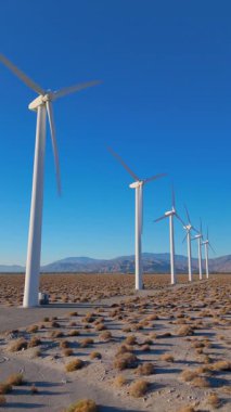 Dikey İHA görüntüleri Palm Springs, Kaliforniya 'nın çöl manzarasında rüzgar türbinlerinin statik görüntülerini gösteriyor. Sabahın erken saatlerinde yakalanan türbinler, berrak bir gökyüzünün altında hareketsiz duruyor.